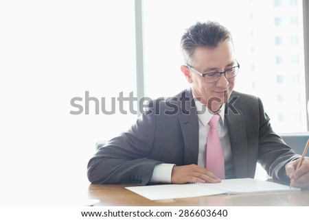 Mature businessman writing on book at table in office