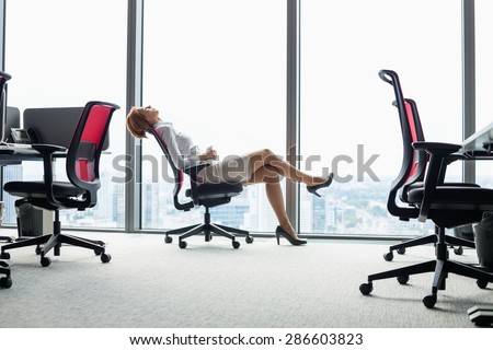 Full length side view of young businesswoman leaning back in chair at office