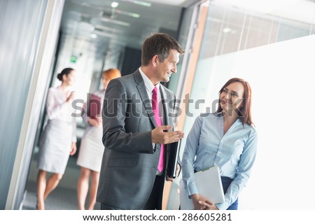 Businessman talking with female colleague while walking in office corridor