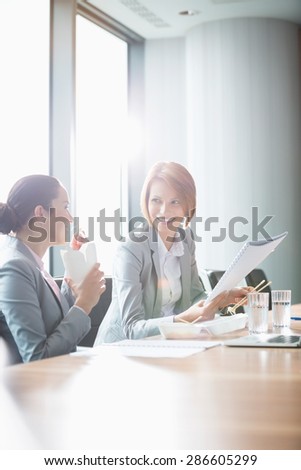 Young businesswomen working while having lunch at table in office