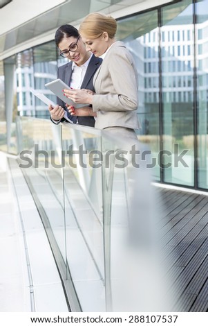 Businesswomen using digital tablet by glass railing