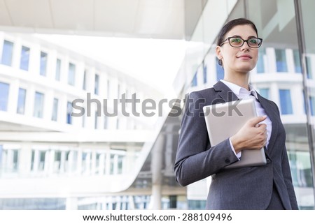 Confident businesswoman holding tablet PC outside office building