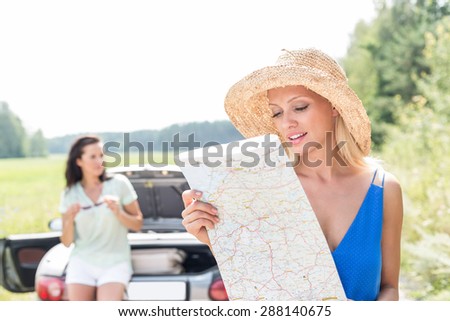 Woman reading map while friend leaning on convertible in background