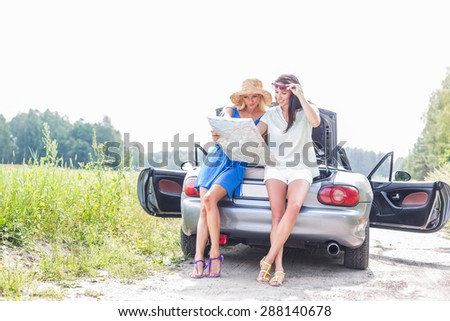 Female friends reading map while leaning on convertible