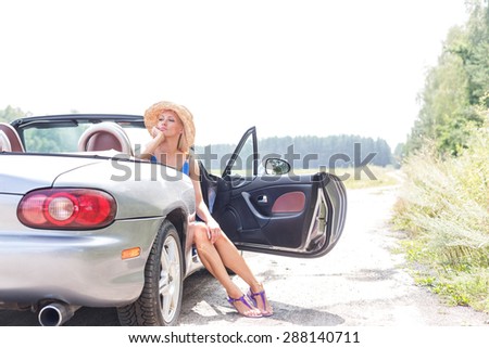 Thoughtful woman sitting in convertible on country road against clear sky