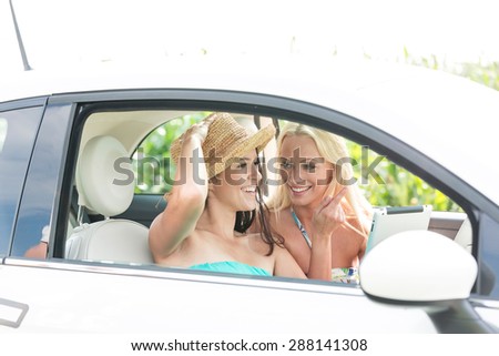 Happy female friends using digital tablet in car on sunny day