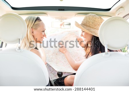 Rear view of happy female friends reading map in car