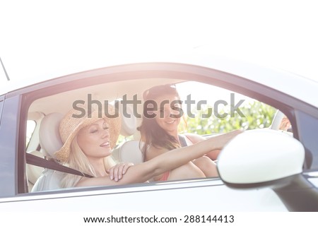 Young female friends in car on sunny day against clear sky