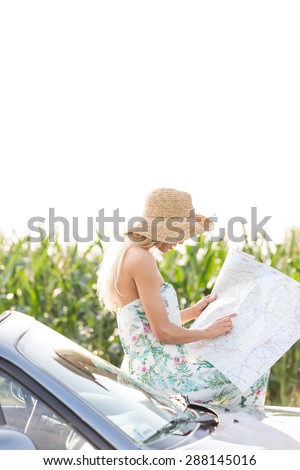 Woman reading map while leaning on convertible against clear sky