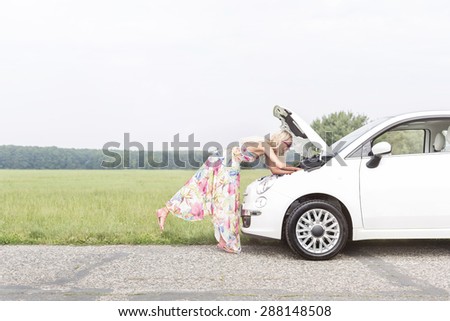 Full-length side view of woman examining broken down car on country road