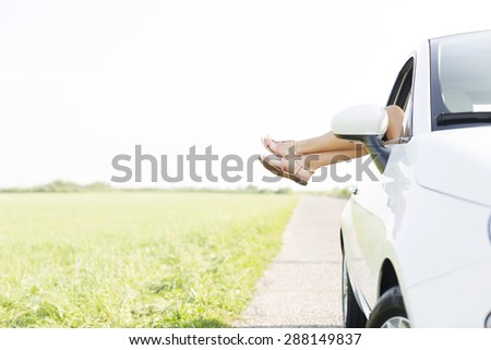 Low section of woman relaxing in car on country road