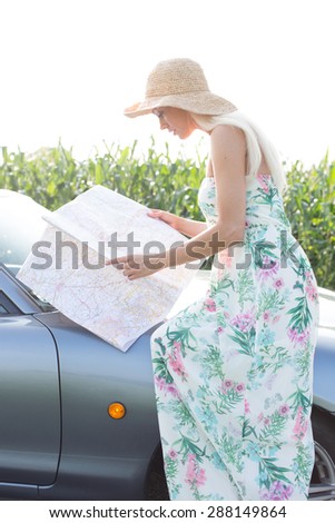 Side view of woman reading map while sitting on convertible