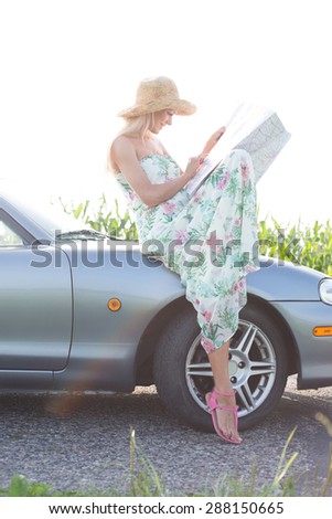 Woman reading map while sitting on convertible