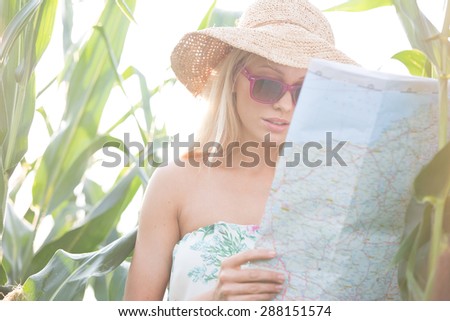 Woman reading map while standing amidst plants outdoors