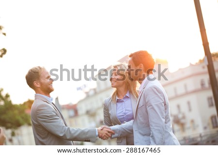 Happy businessmen shaking hands in city against clear sky
