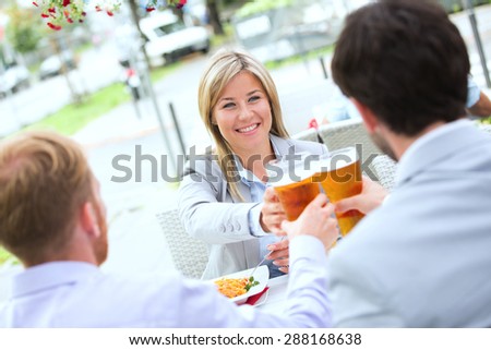 Happy businesswoman toasting beer glass with male colleagues at sidewalk cafe