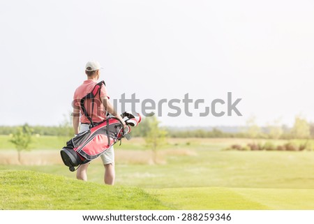Rear view of man carrying golf club bag while walking at course