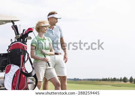 Smiling man and woman standing at golf course against clear sky