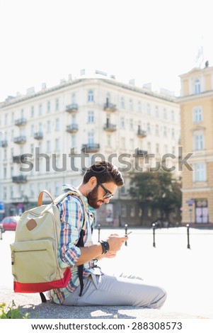 Side view of man with backpack using cell phone in city on sunny day