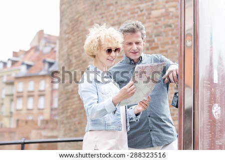 Smiling middle-aged couple reading map in city