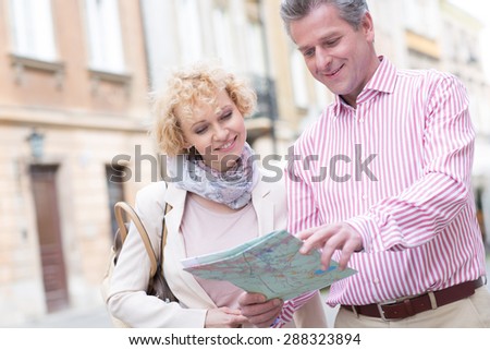 Smiling middle-aged couple reading map in city