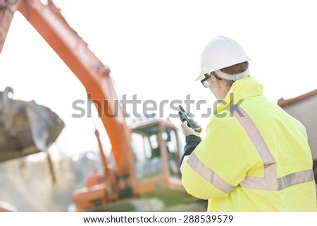 Supervisor using walkie-talkie at construction site against clear sky