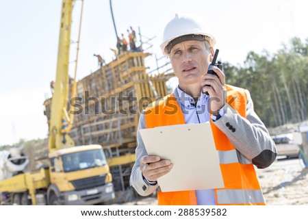 Supervisor using walkie-talkie while holding clipboard at construction site