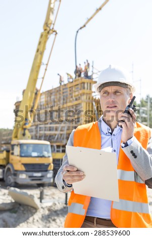 Male supervisor using walkie-talkie while holding clipboard at construction site