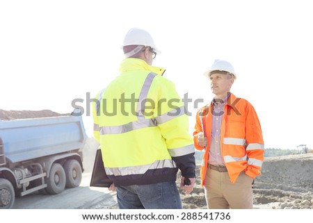 Engineers discussing at construction site against clear sky on sunny day