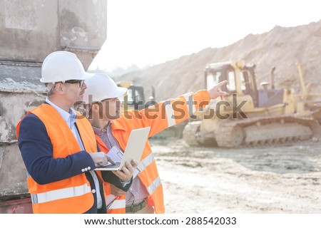 Supervisor showing something to coworker holding laptop at construction site