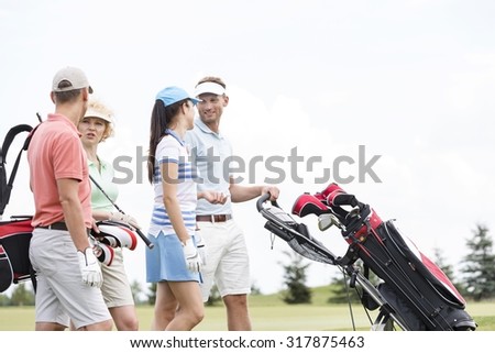 Friends communicating while walking at golf course against clear sky