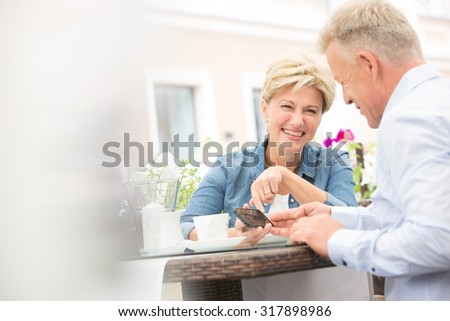 Happy middle-aged couple using mobile phone at sidewalk cafe