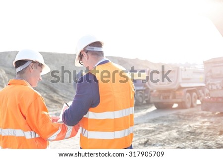 Engineers writing on clipboard at construction site against clear sky
