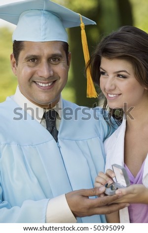 Middle-aged graduate receiving present from daughter outdoors