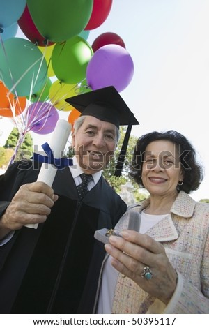 Senior graduate receiving present from wife outside, low angle view
