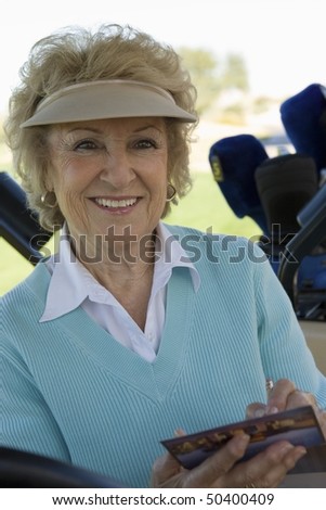 Senior woman holding golf score card, (portrait)