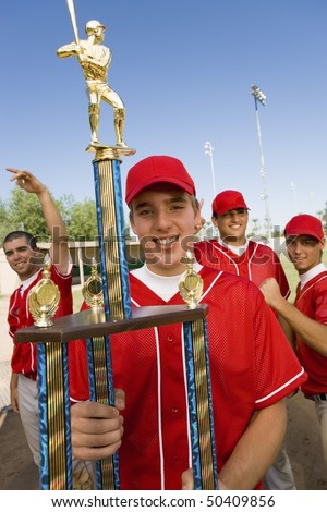 Baseball player holding trophy on field, team-mates in background