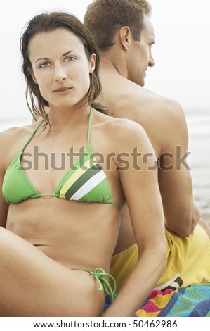 Couple sitting back to back on beach, portrait of woman