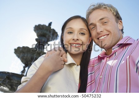 Smiling Couple, arms around, standing in Front of Fountain