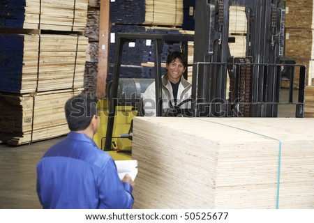 Workers with forklift carrying wood in warehouse