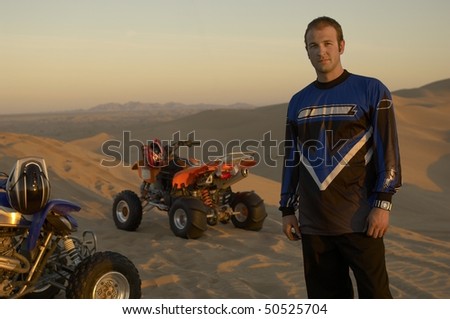 Man standing by quad bikes in desert at sunset