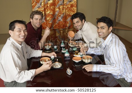 Young men eating sushi with chopsticks in restaurant