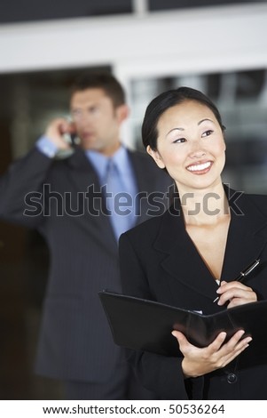 Businesswoman holding folder in front of  businessman using phone