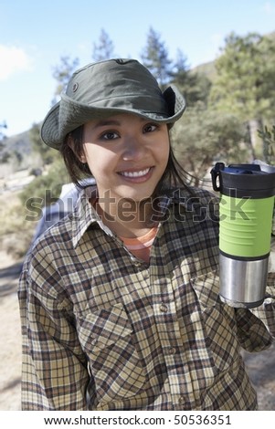 Young woman standing outdoors, holding travel mug.