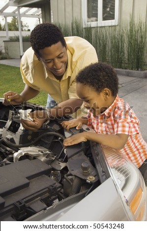 Father and young son inspecting car engine outside house