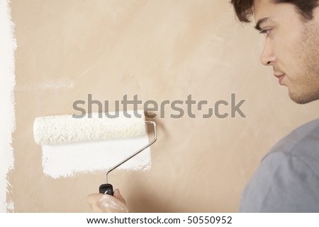 Man painting wall with paint roller, indoors, close up