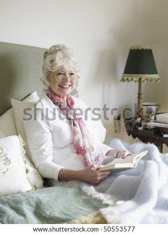 Senior woman sitting on bed, reading book