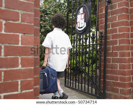 Elementary schoolboy walking through school gate, back view