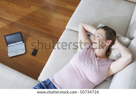 Woman lying down on couch, laptop in background, view from above.