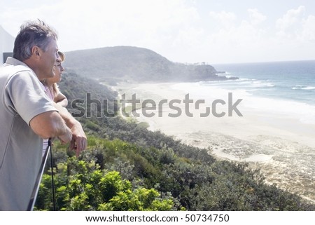 Man and Daughter Looking out at Ocean from balcony of vacation house, side view